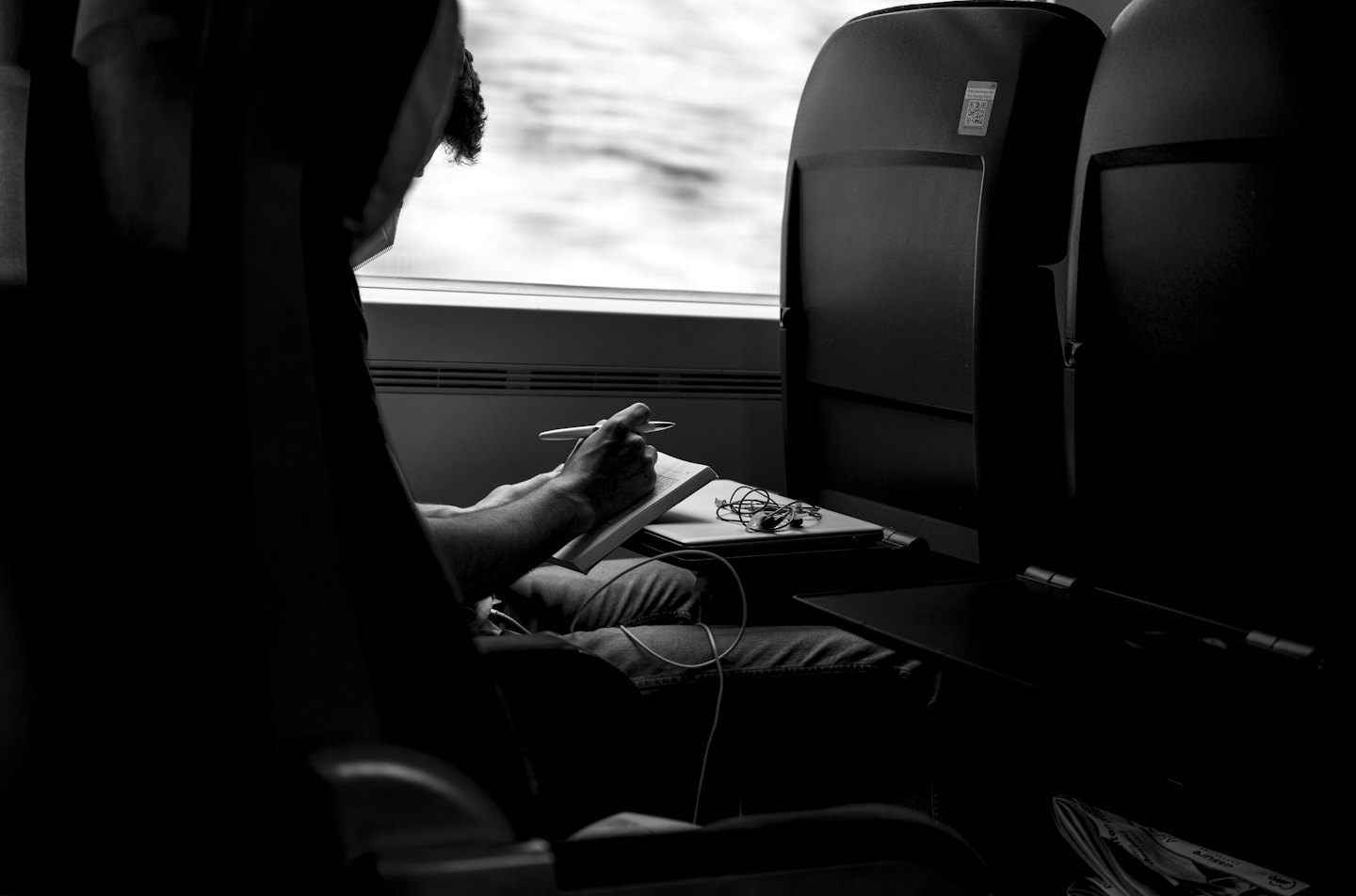 Persona che scrive su un taccuino su un treno con un laptop.